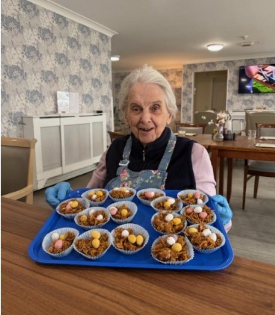 elderly woman holding a blue tray of easter nest cakes