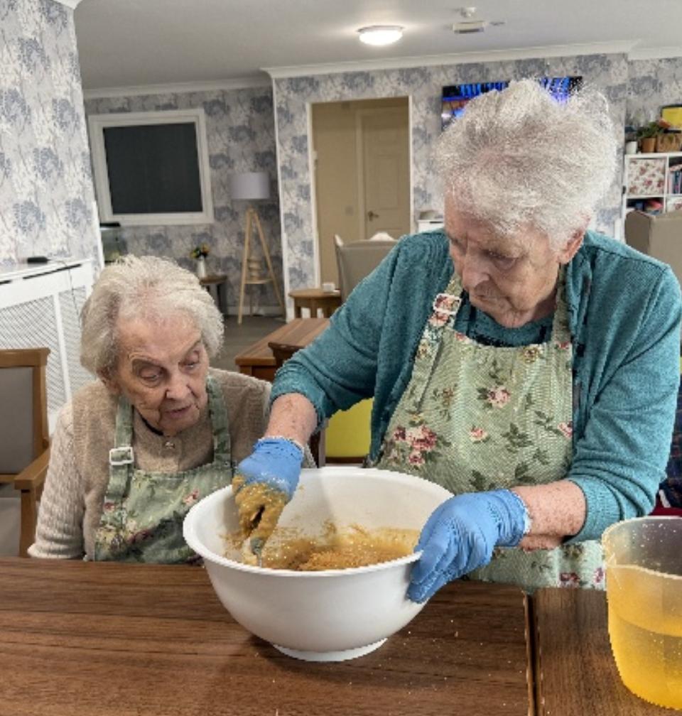 two elderly woman stirring a white bowl of ingredients